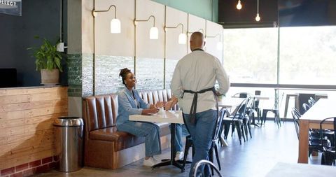 Friendly server greeting customer on leather banquette in modern bright cafe interior