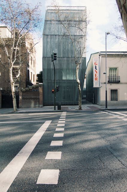 Depicts a modern glass building situated on a quiet urban street. The image captures an intersection and street lights under daylight. Useful for articles on urban planning, architecture, or contemporary city life themes.