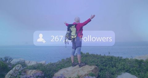 Senior hiker celebrating social media growth on coastal clifftop standing with arms raised