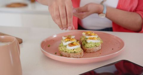 Woman Preparing Avocado Toast with Eggs in Modern Kitchen