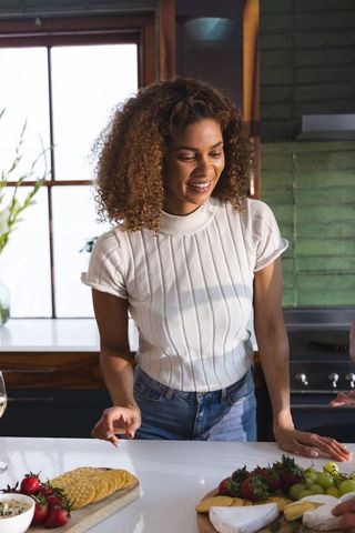 African american woman arranging brie and crackers on cheese board in sunlit home kitchen