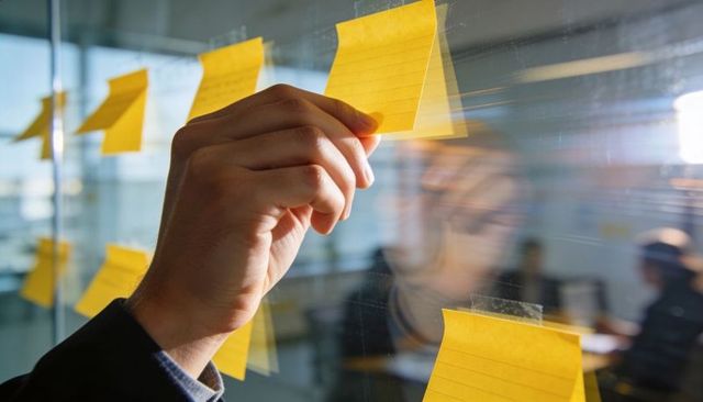 Hand placing yellow sticky note on glass for collaborative brainstorming and planning