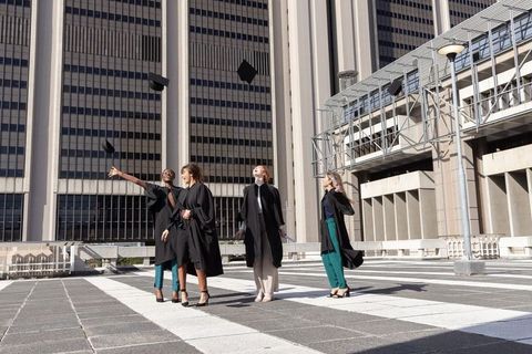 Diverse female graduates celebrating on urban rooftop tossing mortarboards under bright sun