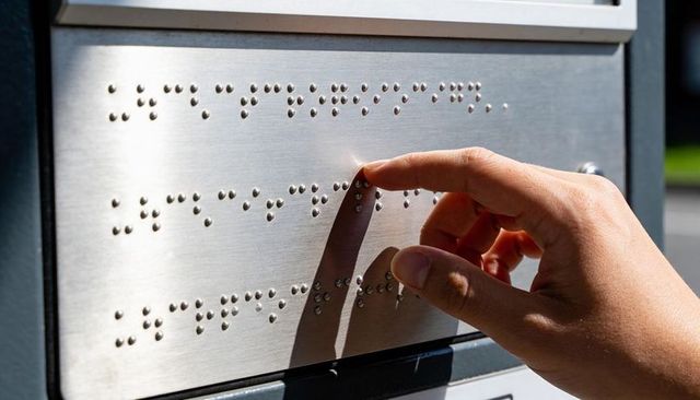 Right hand touching tactile braille panel on brushed aluminum signage for accessibility