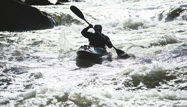 Helmeted kayaker paddling turbulent whitewater rapids through rocky river chute