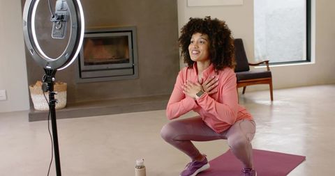 Home fitness instructor filming ring-light workout, squatting on purple yoga mat