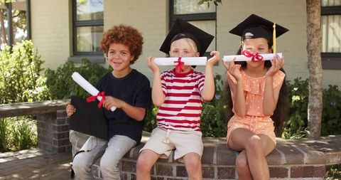 Diverse children celebrating graduation outdoors with caps and diplomas