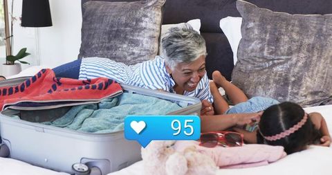 Grandmother laughing while packing suitcase and playing with granddaughter on bed