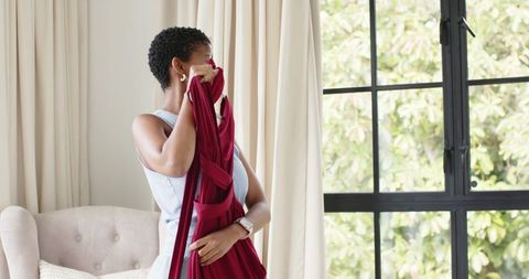 African american woman lifting red dress toward face in sunlit minimalist bedroom