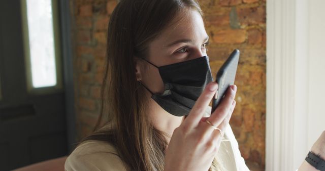 Caucasian female customer wearing face mask, sitting at table, using smartphone. small independent cafe business during coronavirus covid 19 pandemic.