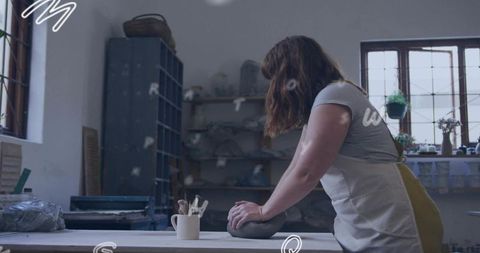 Female potter shaping damp clay on worktable wearing apron with pottery tools