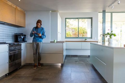 African american man leaning in modern kitchen using tablet for casual remote work