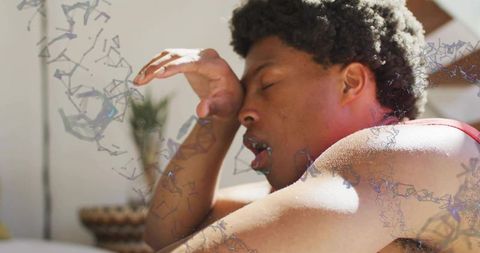 Sunlit man reclining in red tank top rubbing eyes with geometric molecular overlays