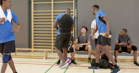 Diverse male volleyball team resting on bench, chatting and hydrating after practice