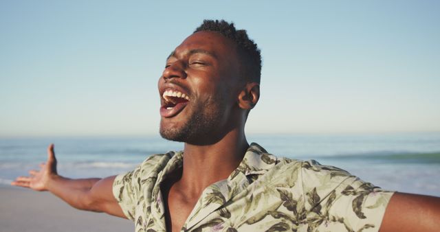 Happy african american man laughing, screaming and raising hands on beach. Summer, relaxation, vacation, happy time.