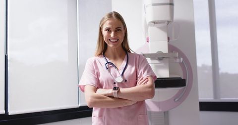 Radiology clinician wearing pink scrubs smiling with mammography unit in modern clinic room