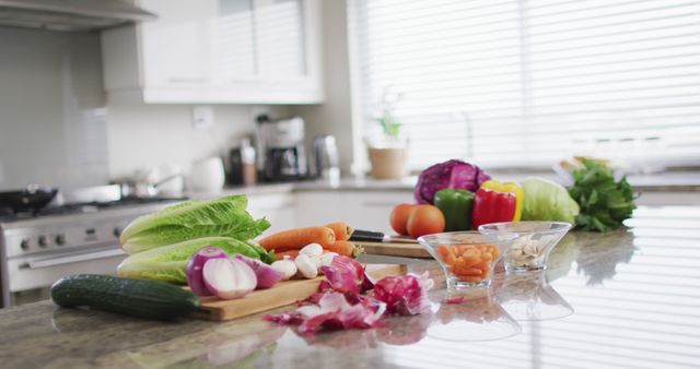 Fresh vegetables like lettuce, carrots, peppers, tomatoes, and onions are arranged on a modern kitchen counter with cutting boards and small bowls. This can be used for articles on healthy eating, meal preparation, home cooking, or kitchen design.
