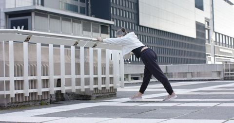Mature woman stretching on urban rooftop railing in athleisure wear