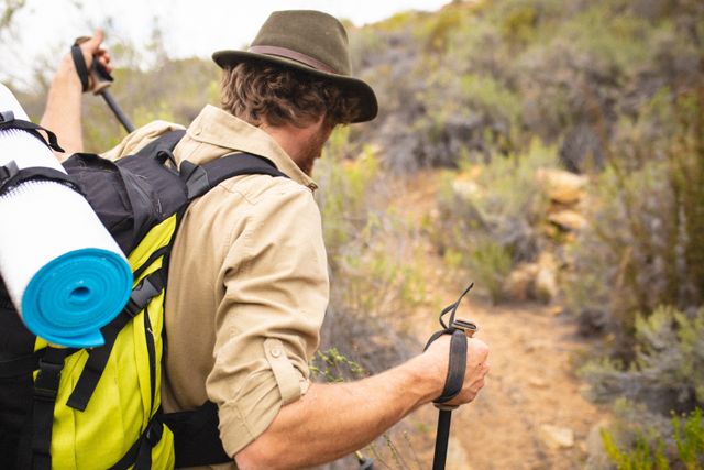 Young male caucasian hiker wearing backpack and hat hiking with poles in wilderness. survivalism and weekend activity, unaltered.