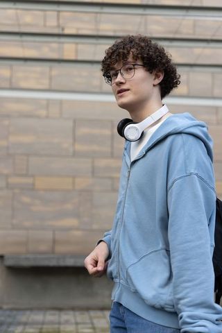 Teen walking on sidewalk wearing blue hoodie and headphones with backpack, student lifestyle
