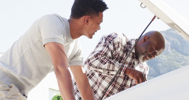 Happy african american father showing adult son how to check oil in car - Download Free Stock Photos Pikwizard.com