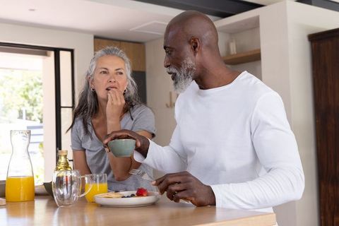 Mature interracial couple enjoying relaxed breakfast at sunlit kitchen island