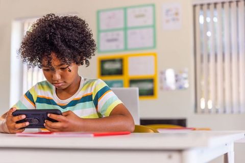 African american boy concentrating on handheld tablet while learning at classroom desk