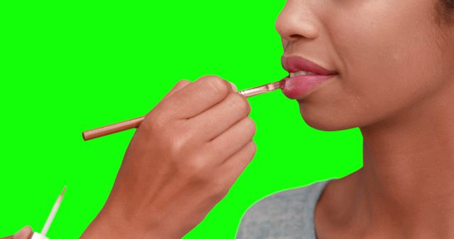 Close-up of woman applying pink lip gloss on vibrant green background - Download Free Stock Photos Pikwizard.com