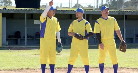 Baseball teammates standing and pointing on infield wearing yellow jerseys and caps