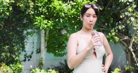 Woman in Swimsuit with Eco Tumbler Sipping Outdoors on Sunny Day