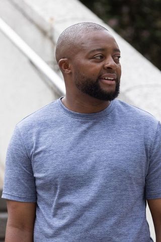 Smiling african man standing on urban stairs wearing blue t-shirt looking right