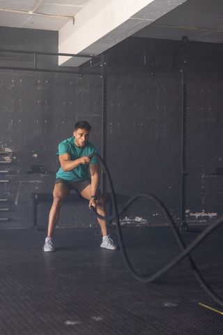 Male Athlete Engaging in Intense Battle Rope Exercise in Gym