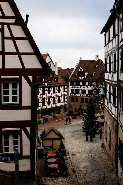 Image depicts a picturesque historic German town with traditional half-timbered houses lining cobblestone streets. People are walking along the quaint paths, with outdoor seating areas visible. Ideal for use in travel blogs, promotional materials for cultural tourism, educational content on European architecture, and travel brochures focusing on traditional and historic locations.