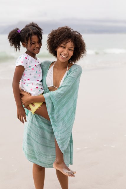 Front view of happy African American mother and daughter standing together at beach on a sunny day