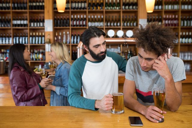 Man offering emotional support to his friend in a bar. Useful for themes related to mental health, friendship, support systems, and social interactions. Can be used in articles, blogs, or advertisements focusing on mental health awareness, the importance of friendships, or bar and pub environments.