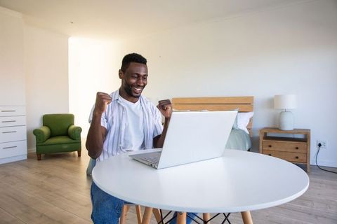 Excited man celebrating success on laptop in bright modern bedroom