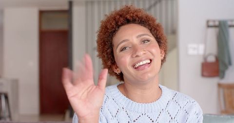 Cheerful Woman Waving and Smiling on Couch in Cozy Living Room