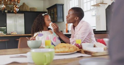 Mother wiping daughter's face during cozy family breakfast at kitchen table morning care