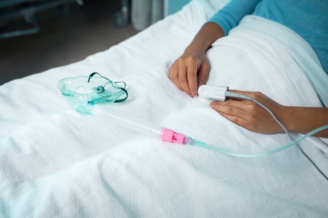 This image depicts a biracial female patient resting in a hospital bed with an oxygen mask nearby. It is suitable for use in medical and healthcare contexts, such as illustrating patient care, hospital environments, or healthcare services. It can be used in articles, brochures, or websites related to medical treatment, patient recovery, and healthcare facilities.