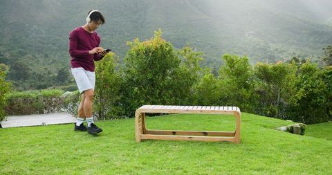 Man with Headphones Checking Phone on Lush Green Lawn