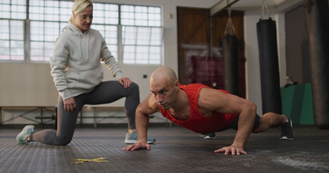 Caucasian muscular man doing push ups with female coach. health and fitness training at gym.