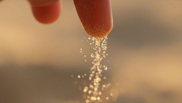 Finger pinching fine beach sand releasing sparkling stream of golden grains macro closeup