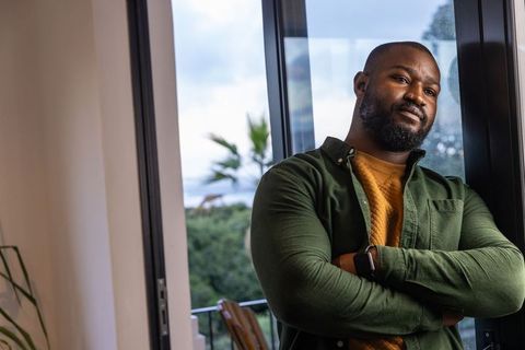 Contemplative african american man standing by rainy balcony glass arms crossed smartwatch