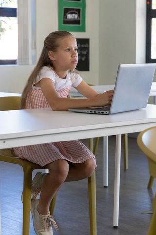 Young student using laptop in bright classroom concentrating on remote learning