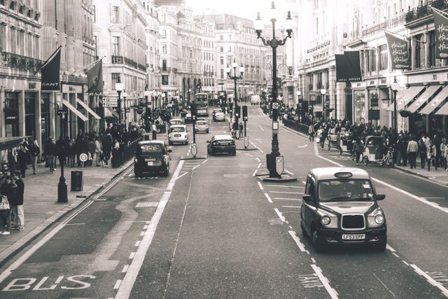 Capturing classic urban life, this image shows a busy street in a European city with black cabs and pedestrians. Historic buildings line the street, providing a timeless feel. This image is perfect for articles or advertisements highlighting city life, transportation, tourism, or urban history.