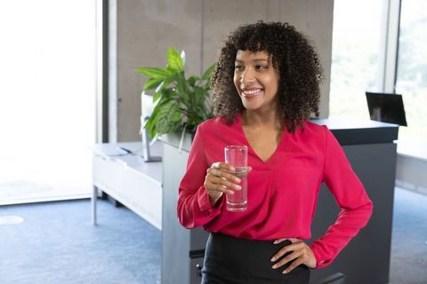 Confident Businesswoman Holding Glass of Water in Modern Office Environment