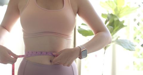 Asian Woman Measuring Waist with Tape in Bright Home Setting