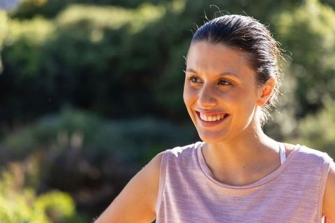 Young woman in 20s smiling outdoors in sunlight wearing mauve tank top, athletic portrait