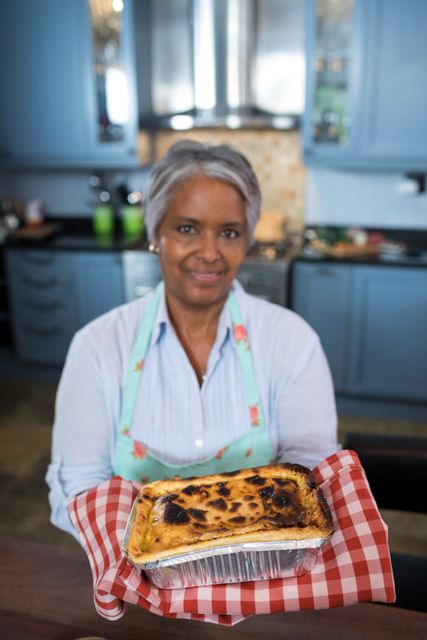 Portrait of senior woman showing baked food while standing in kitchen at home