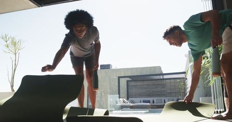 Two men adjusting green exercise mats on modern pool patio holding water bottles